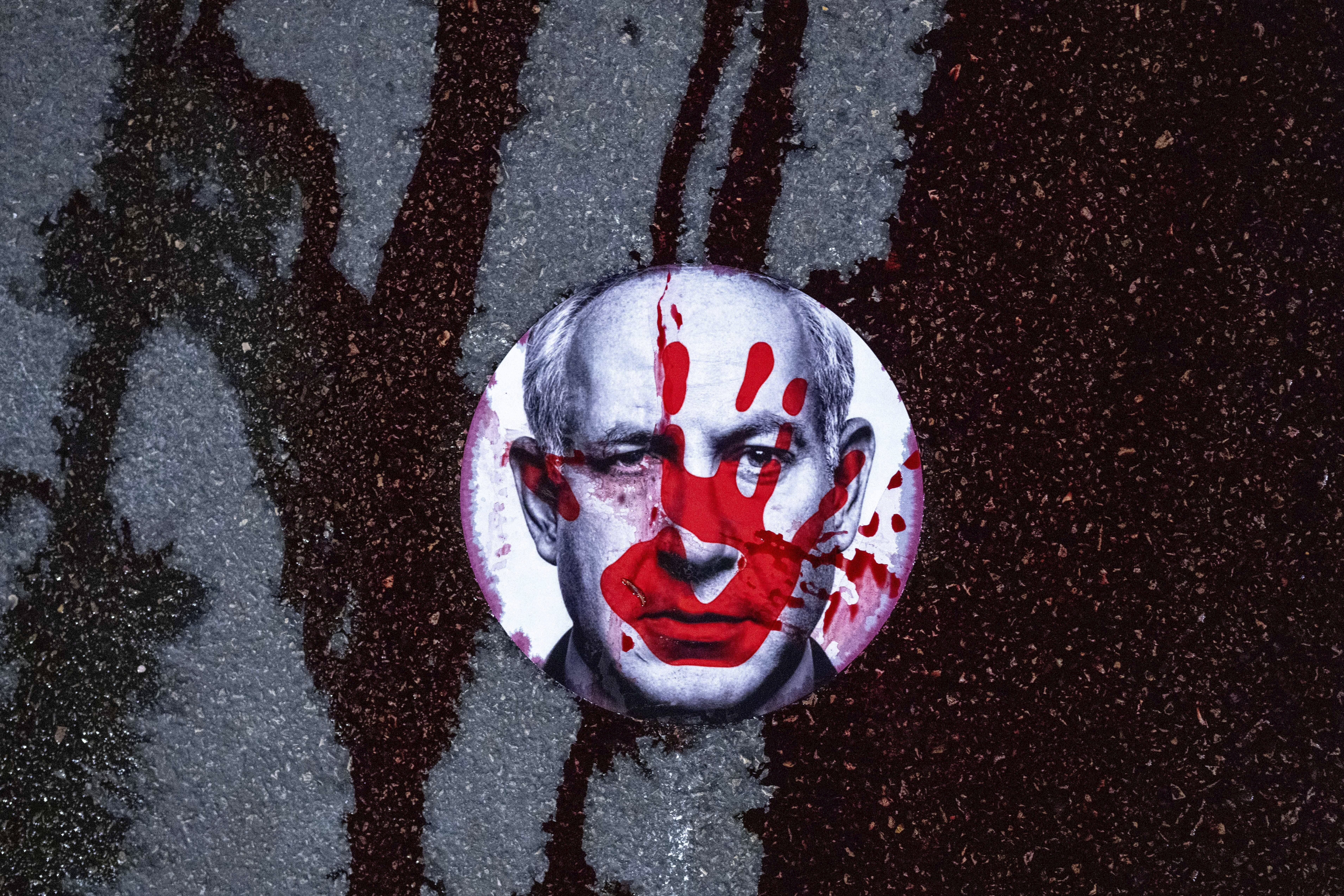 FILE - Supporters of Israelis held hostage by Hamas in Gaza stuck a sticker with the face of Israeli Prime Minister Benjamin Netanyahu on a road and poured red liquid, symbolizing blood, over it, in Jerusalem, Feb. 17, 2025. (AP Photo/Ohad Zwigenberg, File)