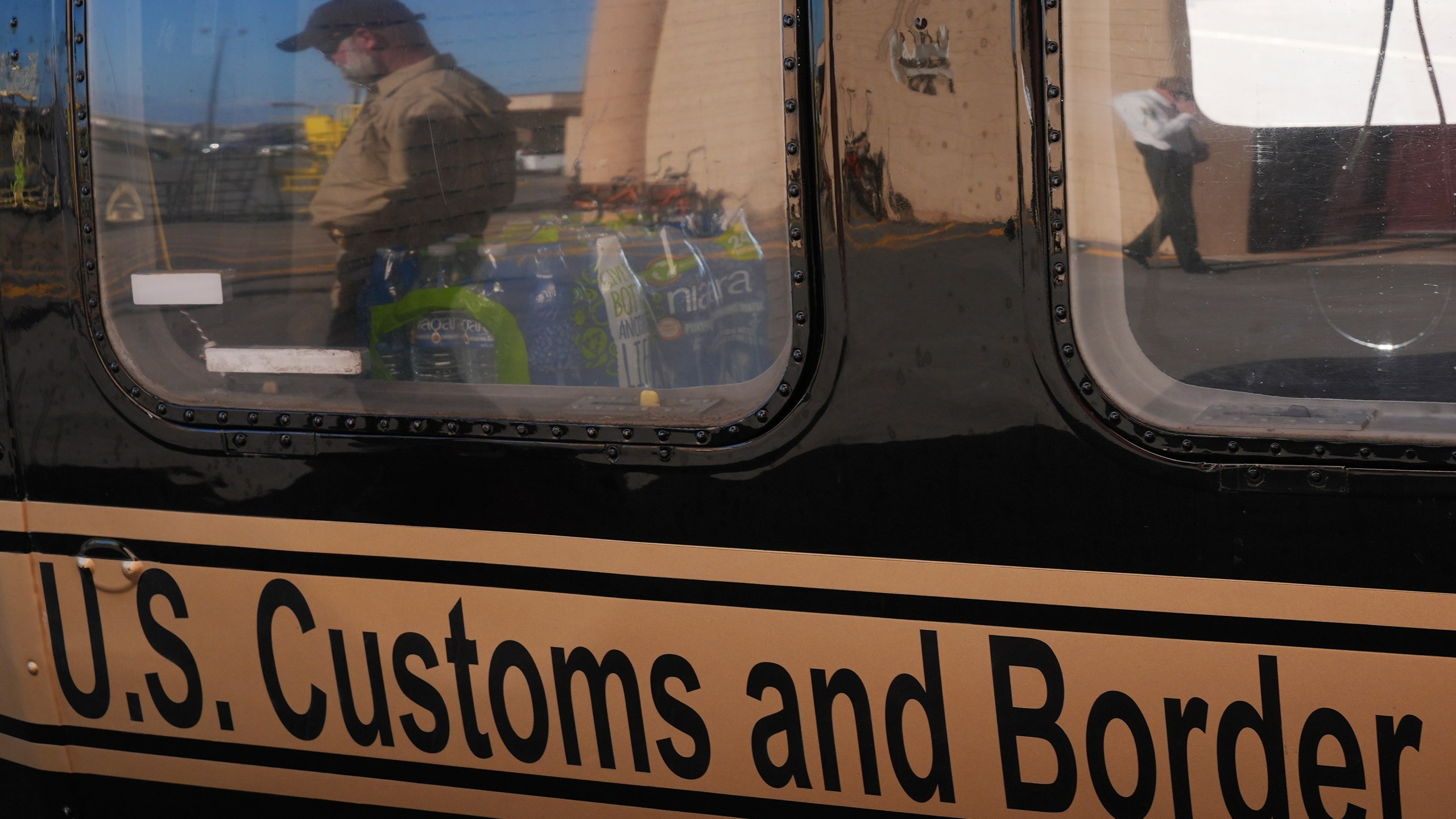 A U.S. Customs and Border Protection agent walking past is reflected in the window of a helicopter at Homestead Air Force Base ahead of a press conference by Florida Gov. Ron DeSantis, Wednesday, Feb. 26, 2025, in Homestead, Fla. (AP Photo/Rebecca Blackwell)