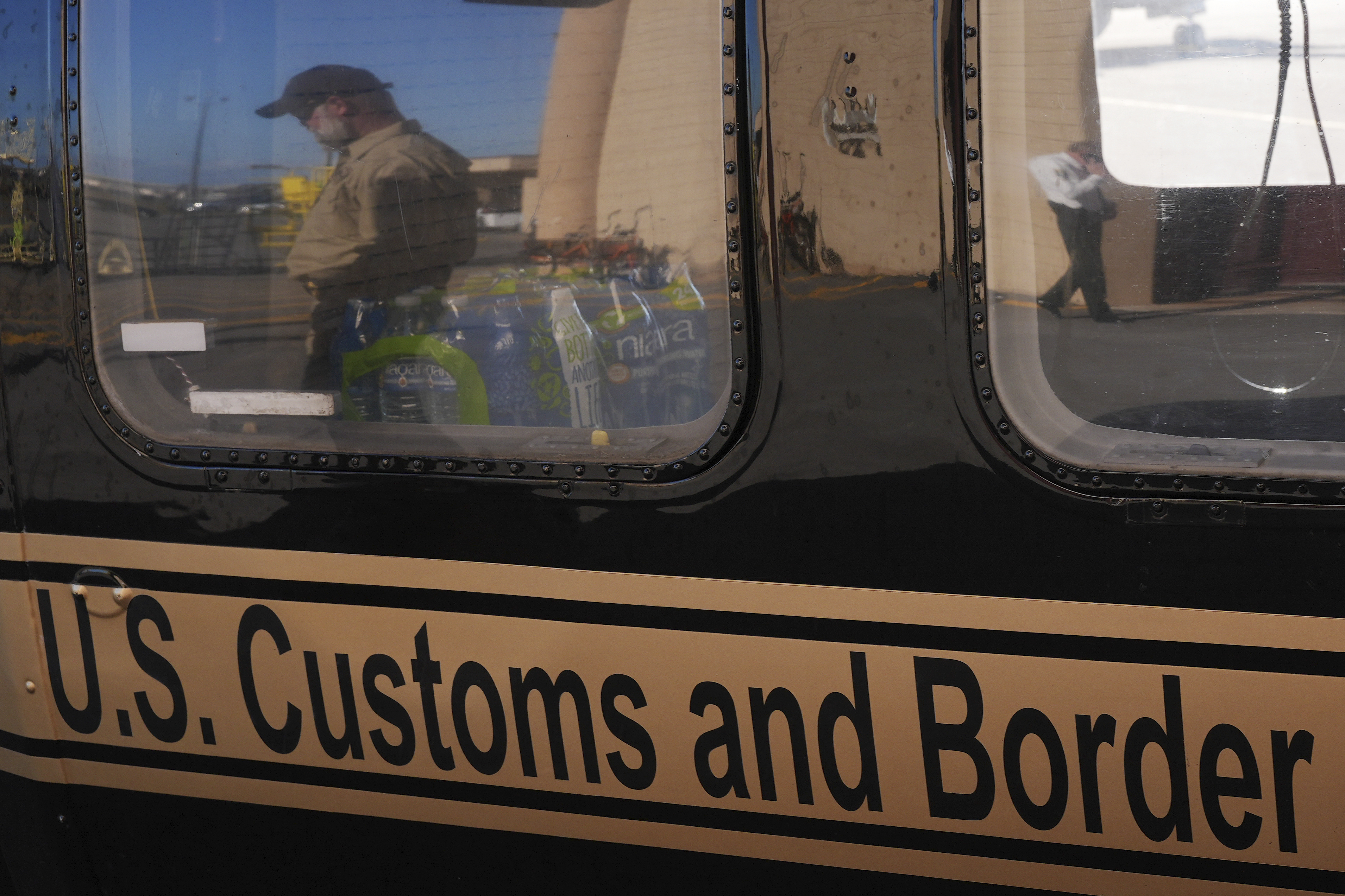 A U.S. Customs and Border Protection agent walking past is reflected in the window of a helicopter at Homestead Air Force Base ahead of a press conference by Florida Gov. Ron DeSantis, Wednesday, Feb. 26, 2025, in Homestead, Fla. (AP Photo/Rebecca Blackwell)