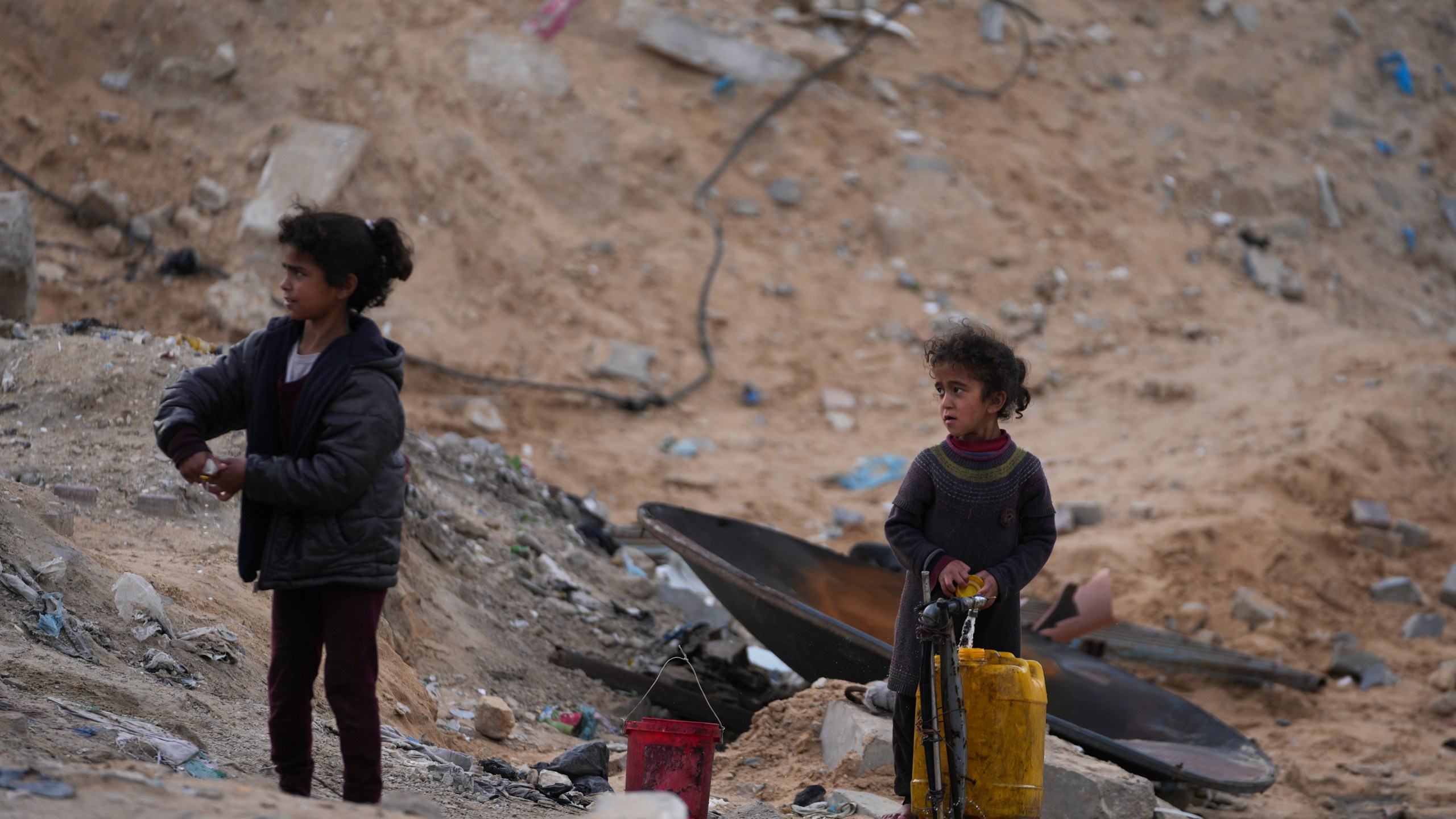 Displaced Palestinians girls fill a plastic jerrycan with water at a school run by UNRWA, the U.N. agency helping Palestinian refugees, which they use as a shelter west of Gaza City, Sunday, March 9, 2025. (AP Photo/Jehad Alshrafi)