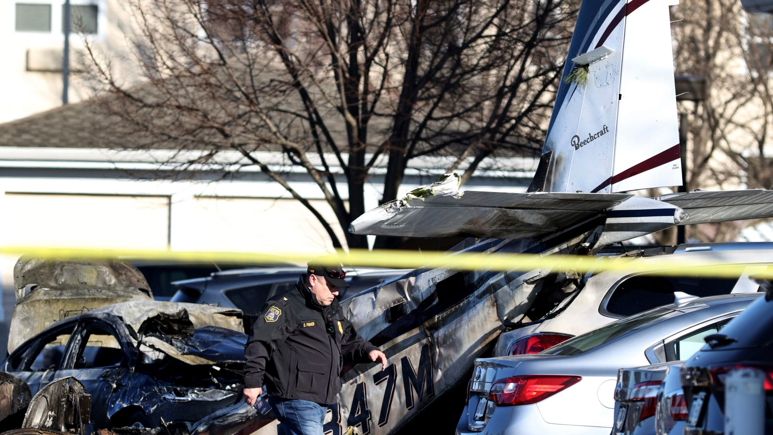 A police officer walks past debris after a plane crashed in a parking lot of a retirement community Sunday, March 9, 2025, in Manheim Township, Pa. (Zach Gleiter/The Patriot-News via AP)