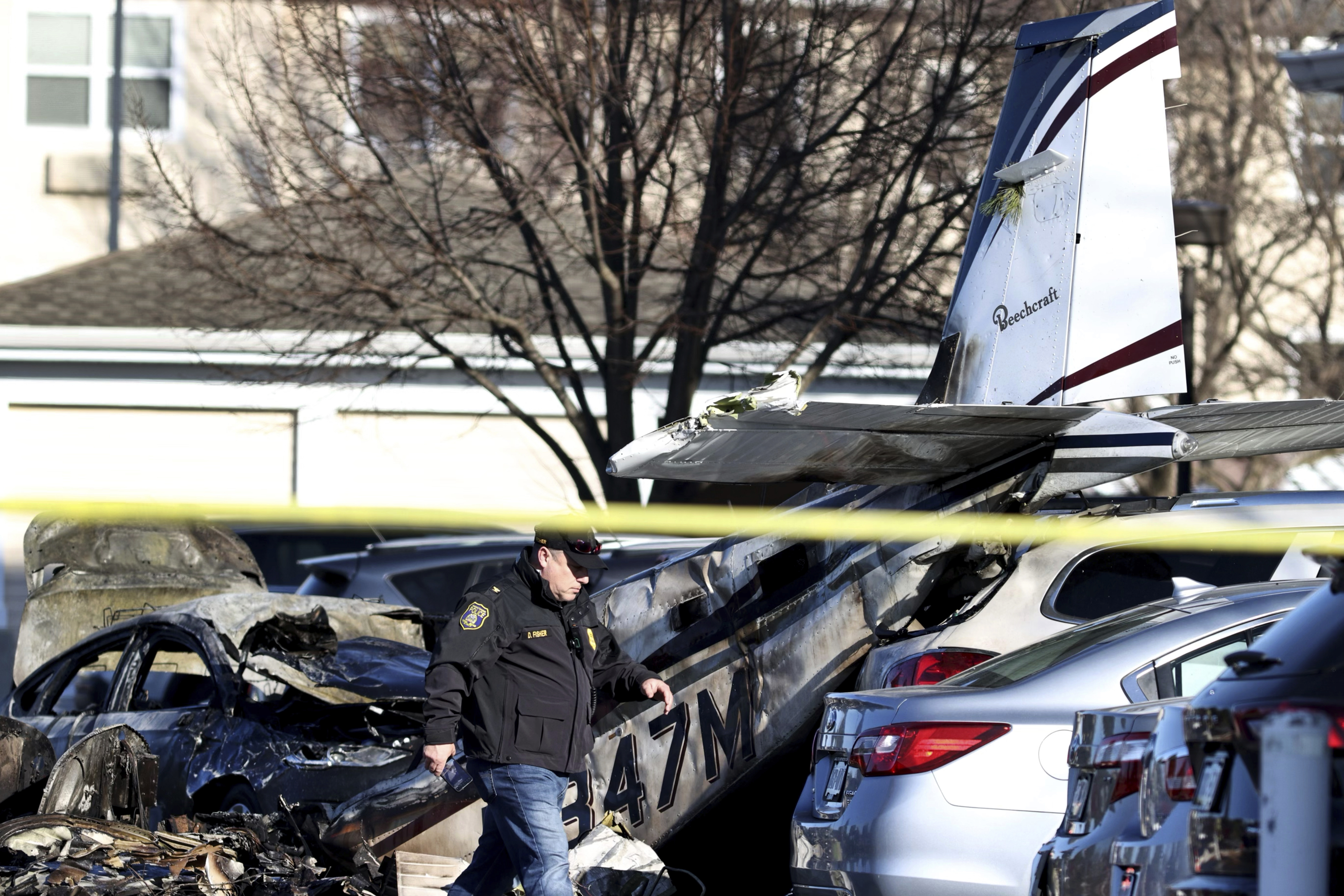 A police officer walks past debris after a plane crashed in a parking lot of a retirement community Sunday, March 9, 2025, in Manheim Township, Pa. (Zach Gleiter/The Patriot-News via AP)