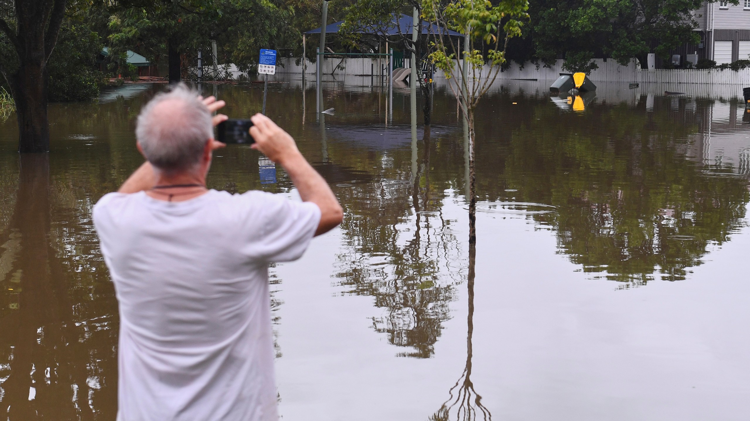 A resident takes photos of a flooded road, in Oxley, in Brisbane, Australia, Monday, March 10, 2025. (Jono Searle/AAP Image via AP)