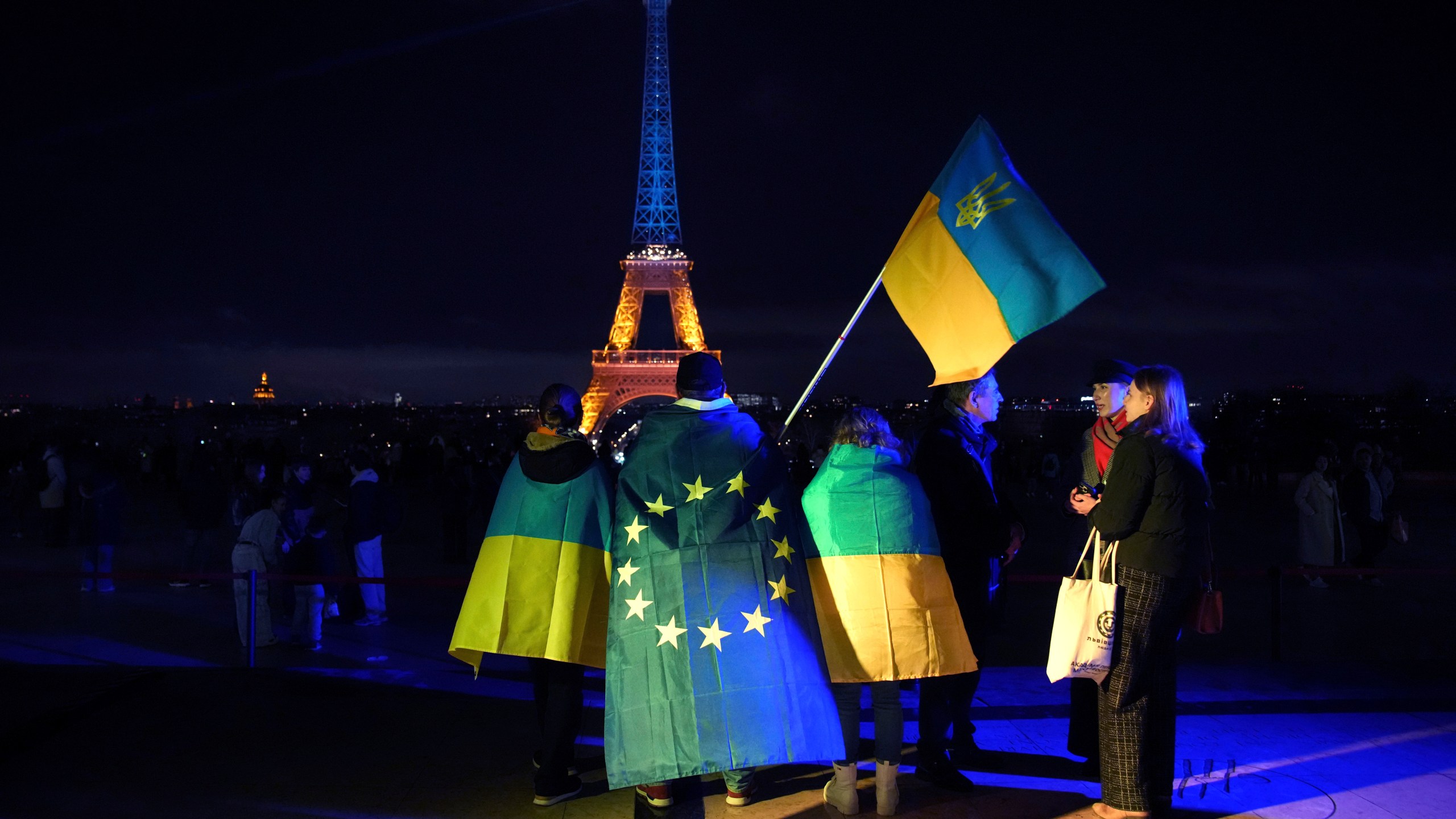 FILE - Ukrainians hold Ukrainian and European flag as the Eiffel Tower is illuminated with the colors of Ukraine to mark the third anniversary of Russia's invasion of the country, in Paris, Monday, Feb. 24, 2025. (AP Photo/Christophe Ena, file)