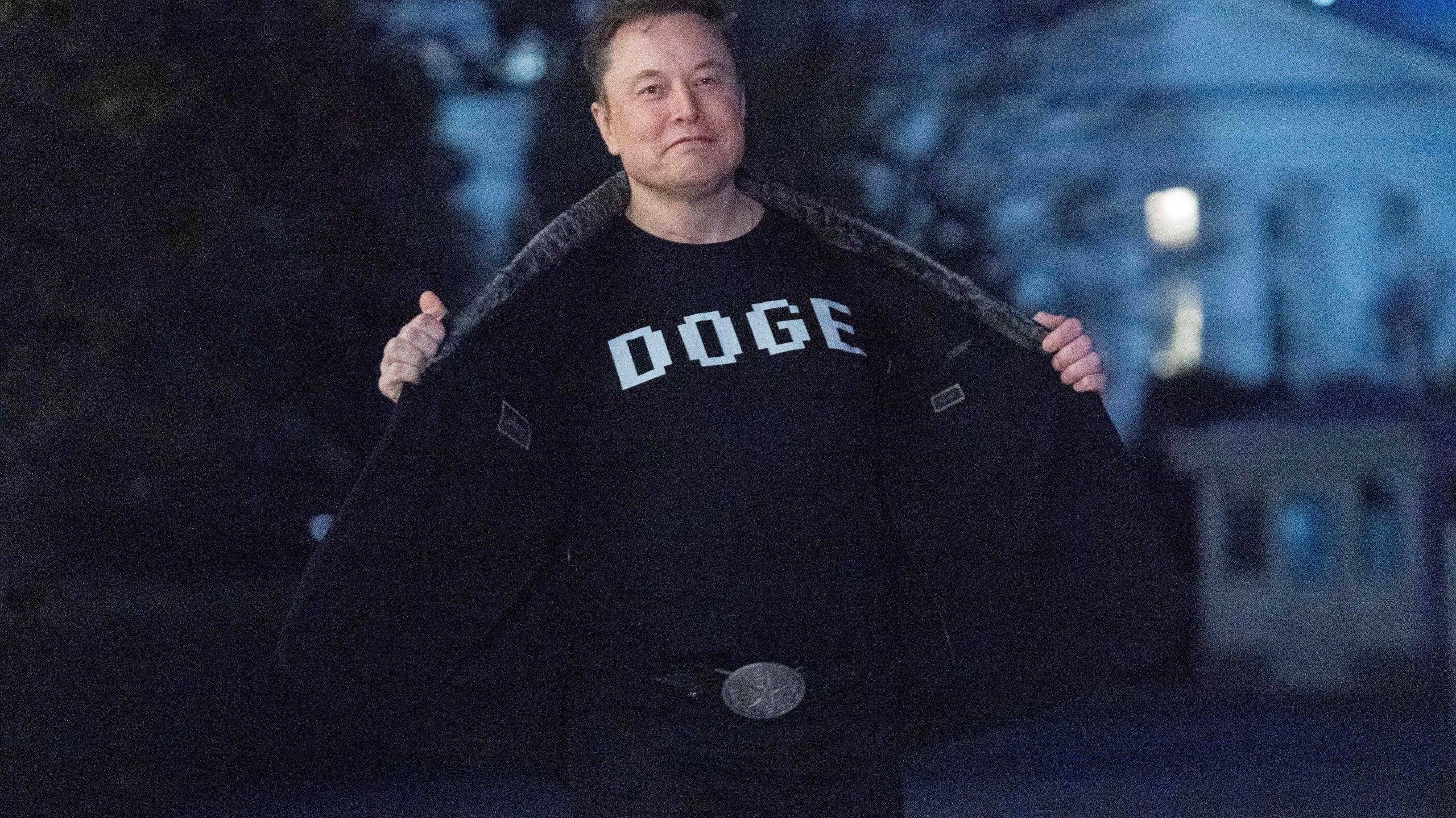 Elon Musk flashes his t-shirt that reads "DOGE" to the media as he walks on South Lawn of the White House, in Washington, Sunday, March 9, 2025. (AP Photo/Jose Luis Magana)