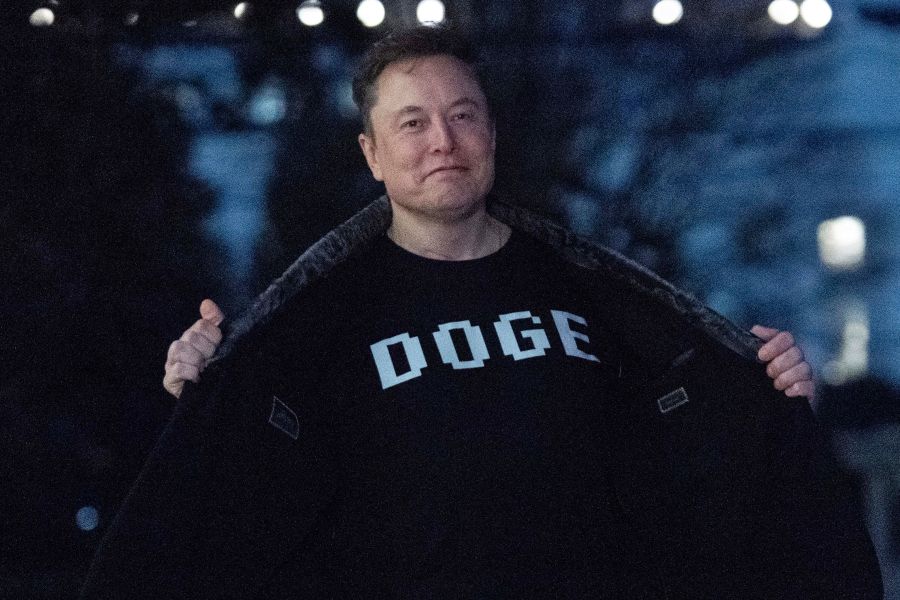 Elon Musk flashes his t-shirt that reads "DOGE" to the media as he walks on South Lawn of the White House, in Washington, Sunday, March 9, 2025. (AP Photo/Jose Luis Magana)