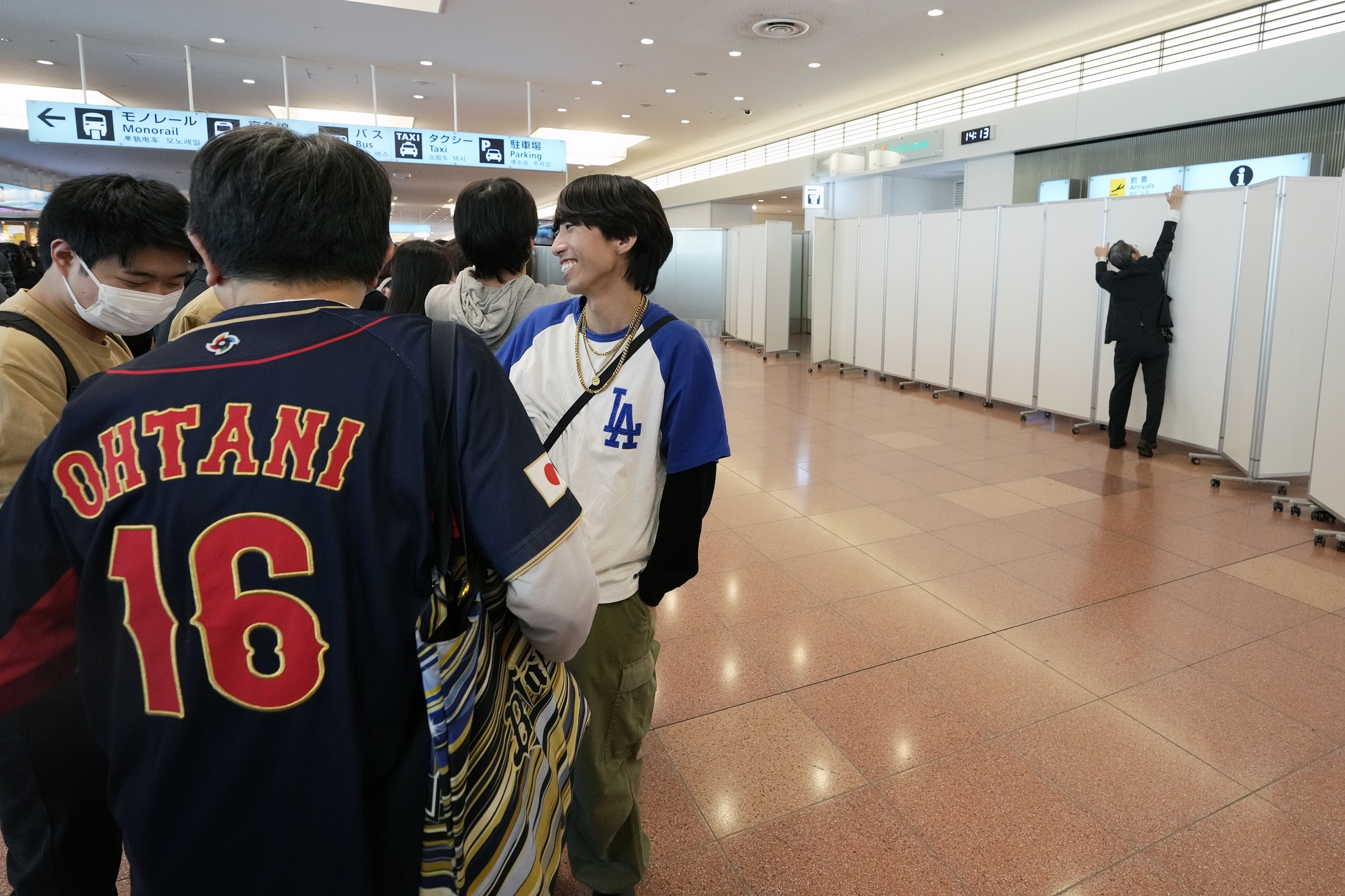 Fans of Los Angeles Dodgers wait for the team arrival as a staff installs partitions to block fans from the arrival route of the Dodgers team members at Tokyo International Airport Thursday, March 13, 2025, in Tokyo, as Dodgers to play their MLB opening games against and Chicago Cubs in Tokyo on March 18-19. (AP Photo/Hiro Komae)