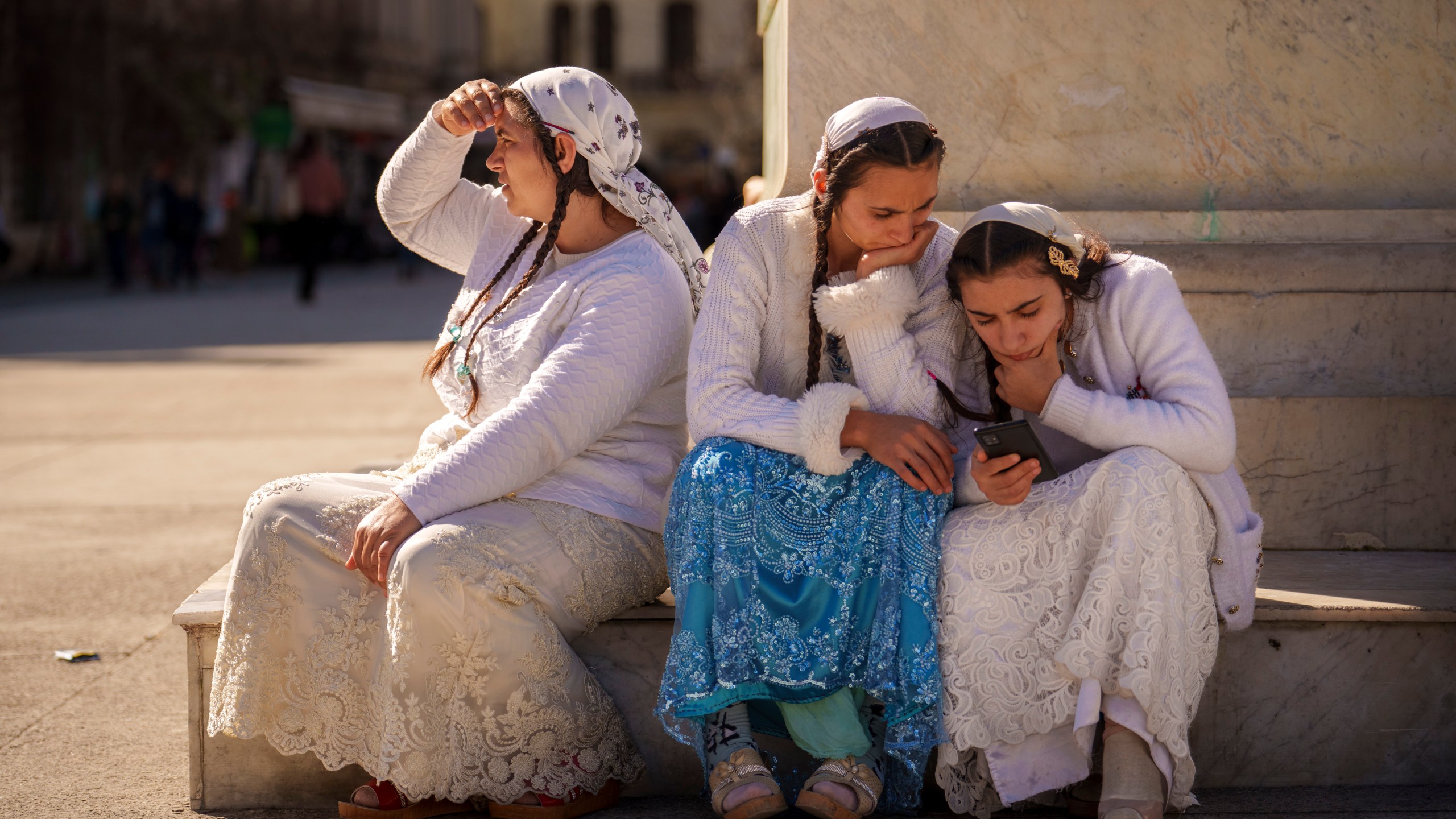 Women look at a phone while sitting on the pedestal of statue on International Women's Day in downtown Bucharest, Romania, Saturday, March 8, 2025. (AP Photo/Vadim Ghirda)