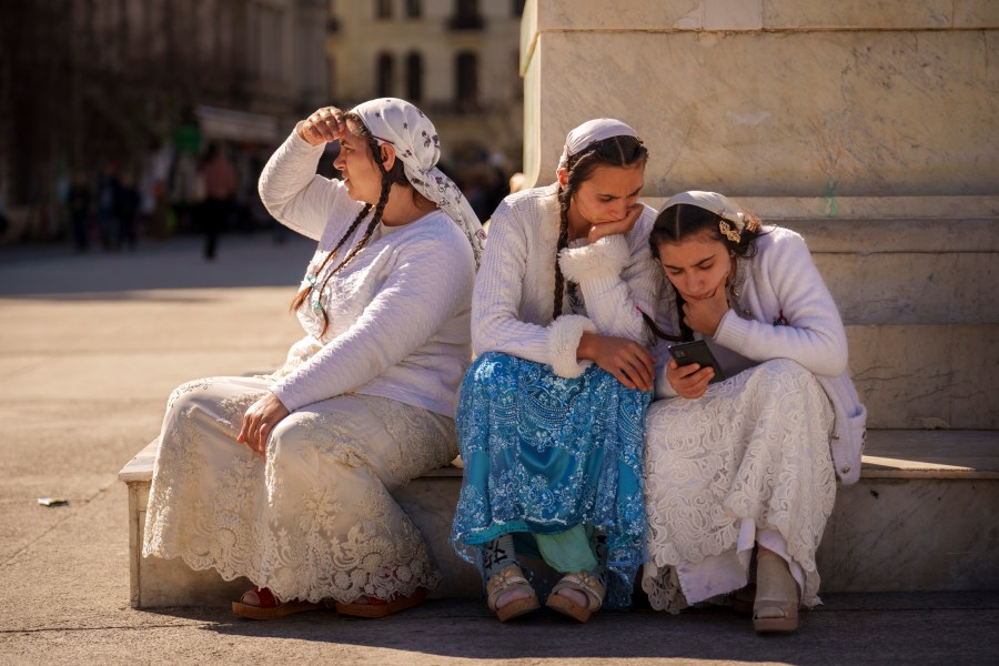 Women look at a phone while sitting on the pedestal of statue on International Women's Day in downtown Bucharest, Romania, Saturday, March 8, 2025. (AP Photo/Vadim Ghirda)