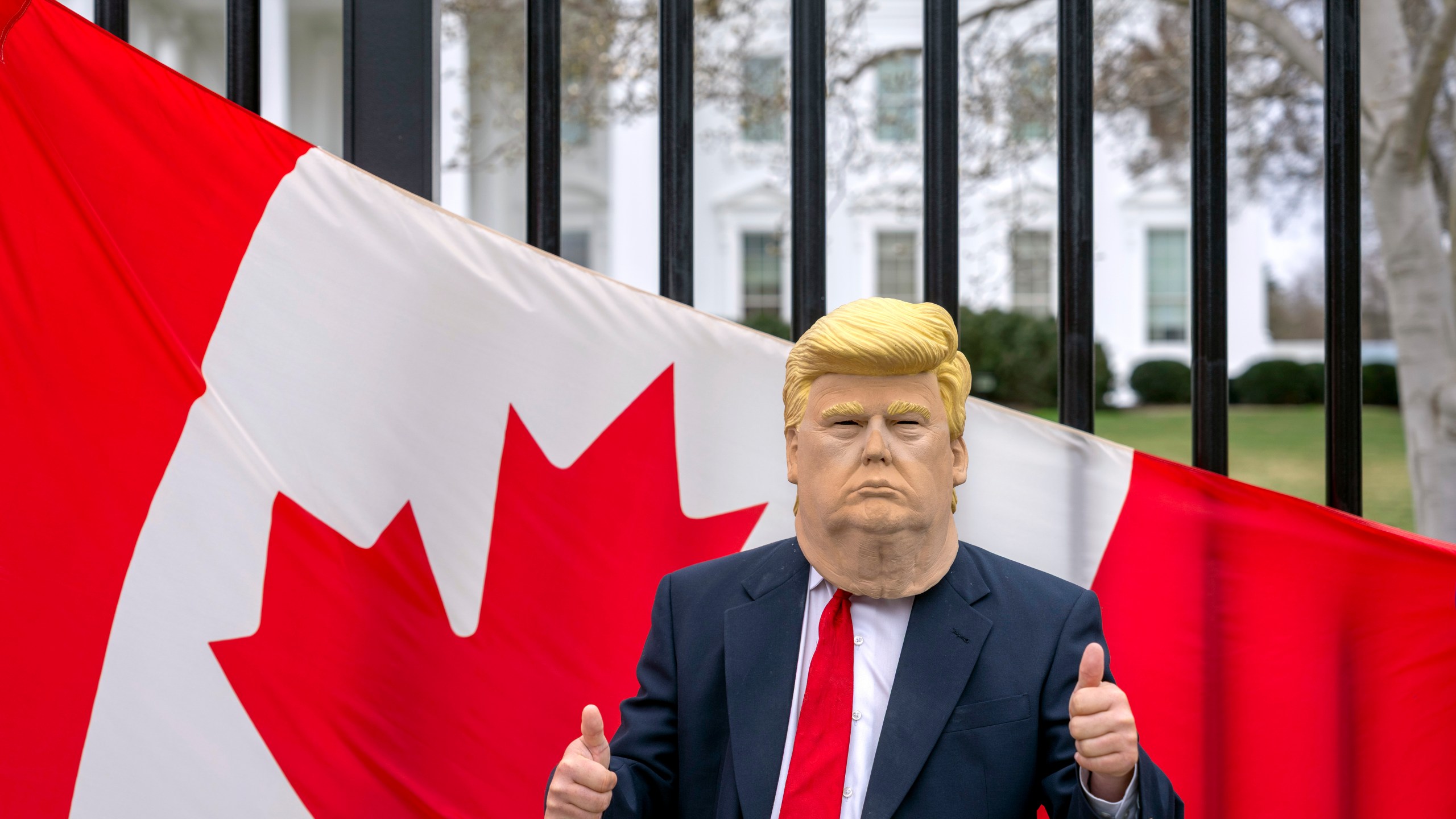 A visitor to the city wearing a mask of President Donald Trump poses for a photo in front of a Canadian flag being held by tourists from Toronto showing their support for Canada regarding trade tariffs, in front of the White House in Washington, Thursday, March 13, 2025. (AP Photo/Ben Curtis)