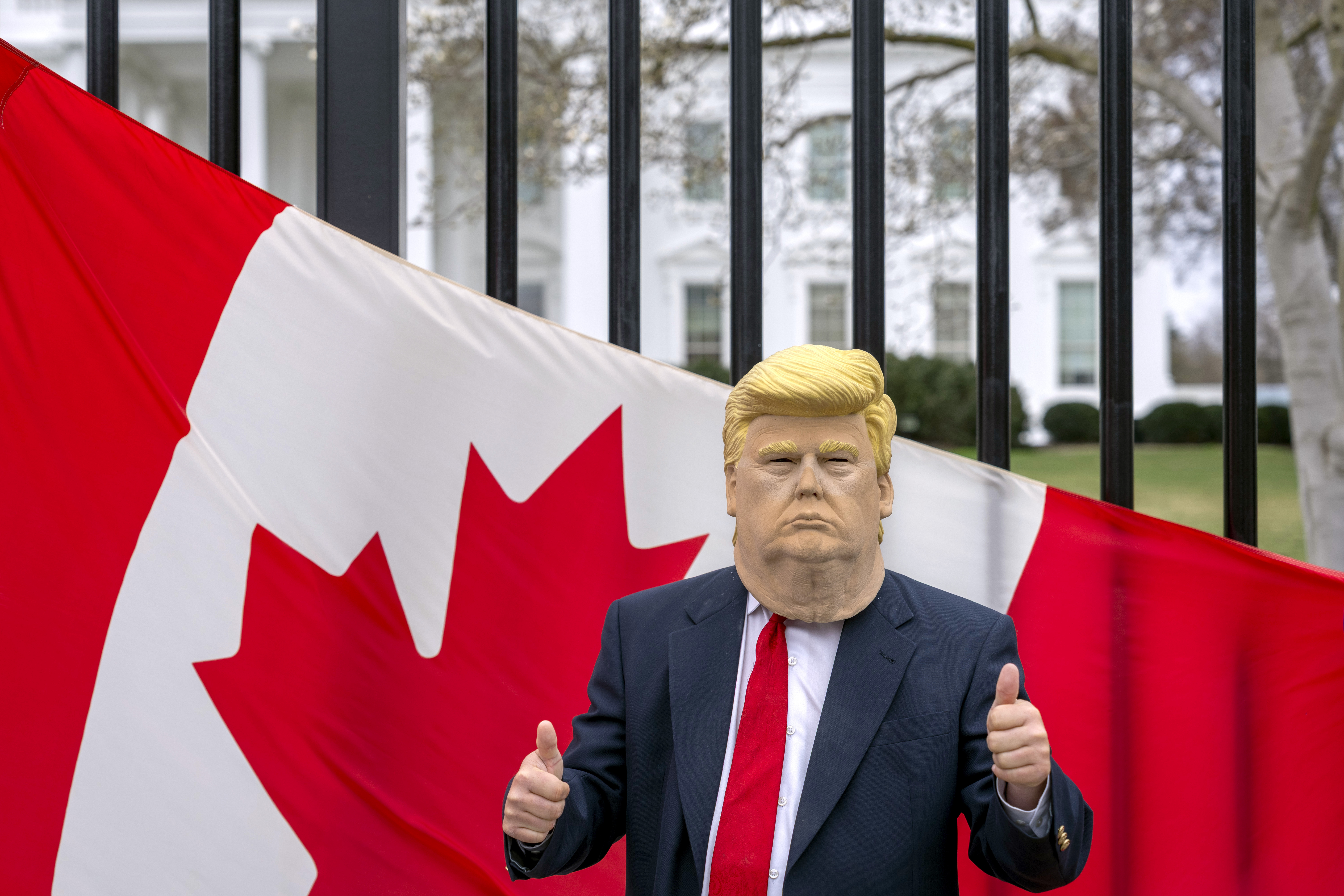 A visitor to the city wearing a mask of President Donald Trump poses for a photo in front of a Canadian flag being held by tourists from Toronto showing their support for Canada regarding trade tariffs, in front of the White House in Washington, Thursday, March 13, 2025. (AP Photo/Ben Curtis)