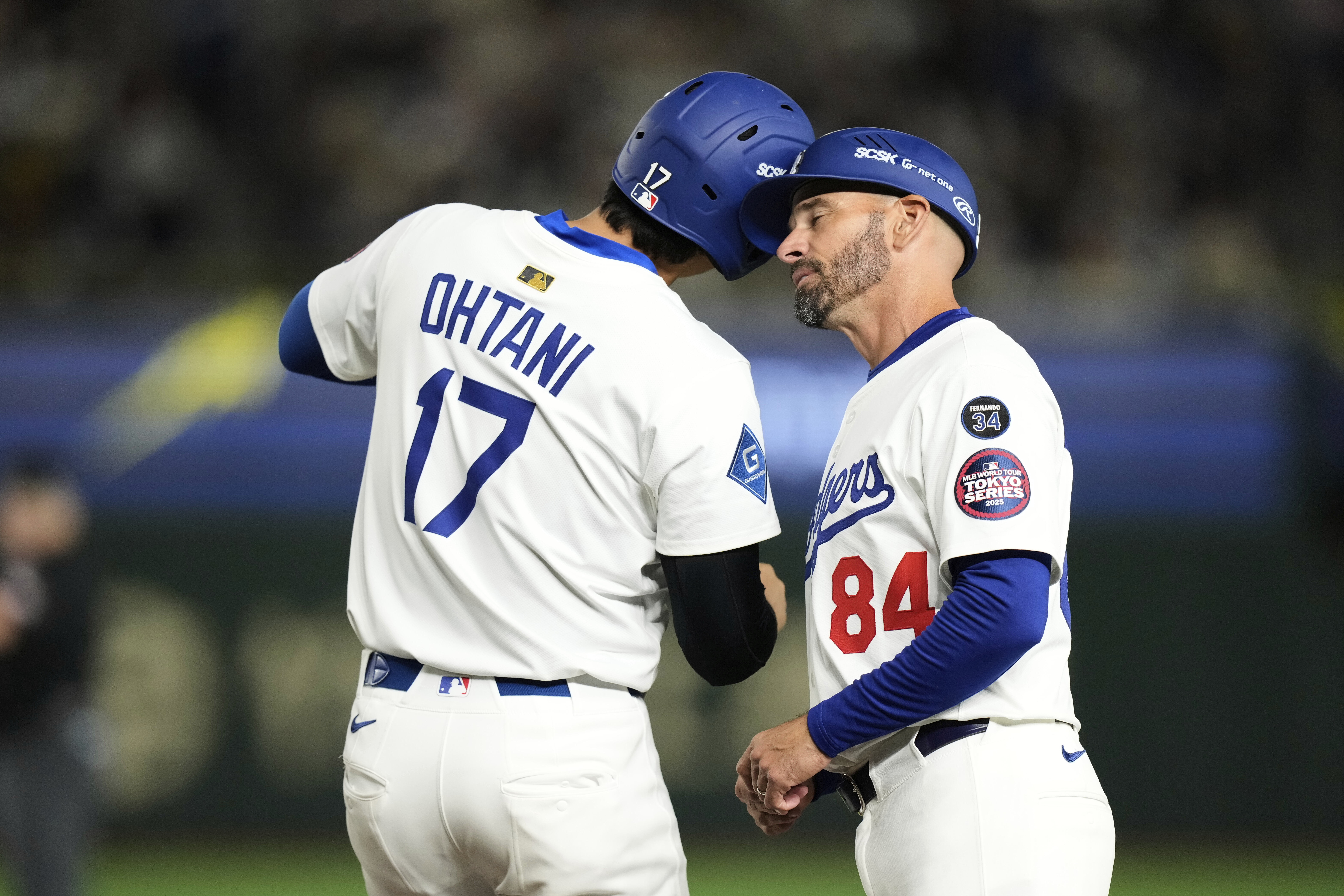 Los Angeles Dodgers' Shohei Ohtani, left, and first base coach Chris Woodward, right, greet each other after Ohtani earned a walk in the first inning of a spring training baseball game against the Yomiuri Giants in Tokyo, Japan, Saturday, March 15, 2025. (AP Photo/Hiro Komae)