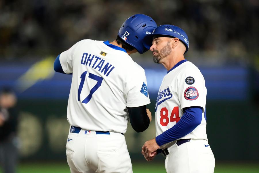 Los Angeles Dodgers' Shohei Ohtani, left, and first base coach Chris Woodward, right, greet each other after Ohtani earned a walk in the first inning of a spring training baseball game against the Yomiuri Giants in Tokyo, Japan, Saturday, March 15, 2025. (AP Photo/Hiro Komae)