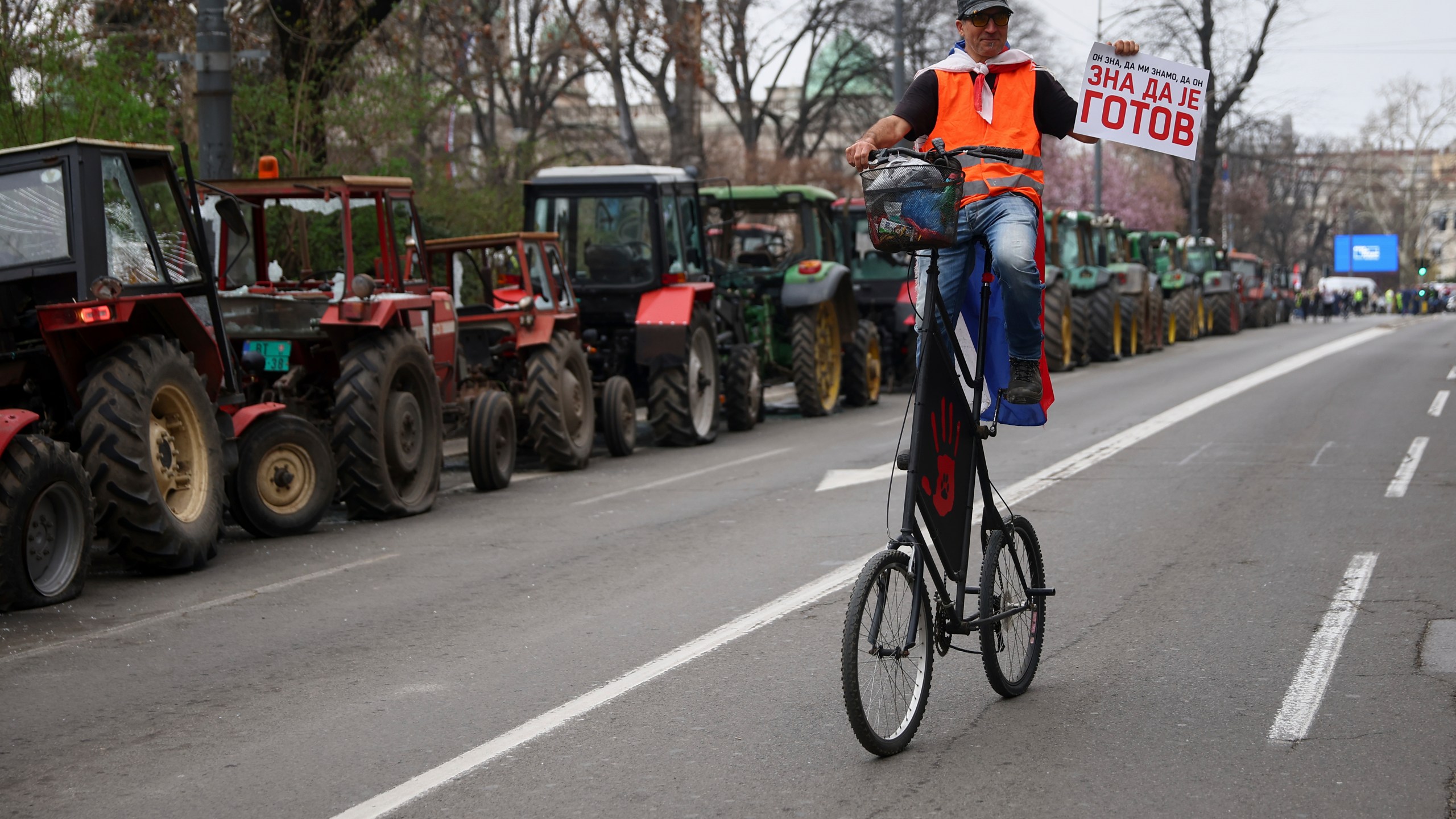 A protester riding past parked tractors carries a placard reading 'he knows he is done' during a major rally against populist President Aleksandar Vucic and his government, in downtown Belgrade, Serbia, Saturday, March 15, 2025. (AP Photo/Armin Durgut)