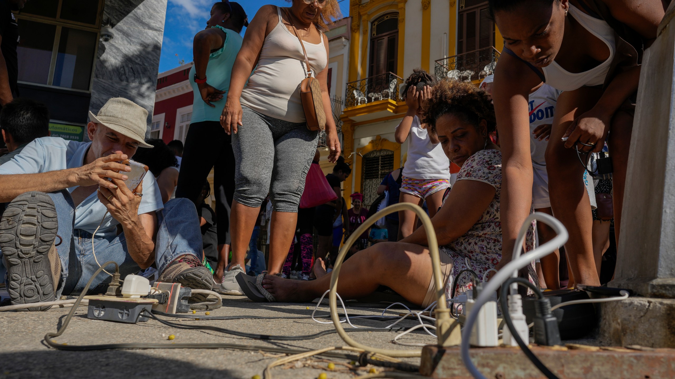 Residents charge their electronic devices on a street during a general blackout in Havana, Saturday, March 15, 2025. (AP Photo/Ramon Espinosa)