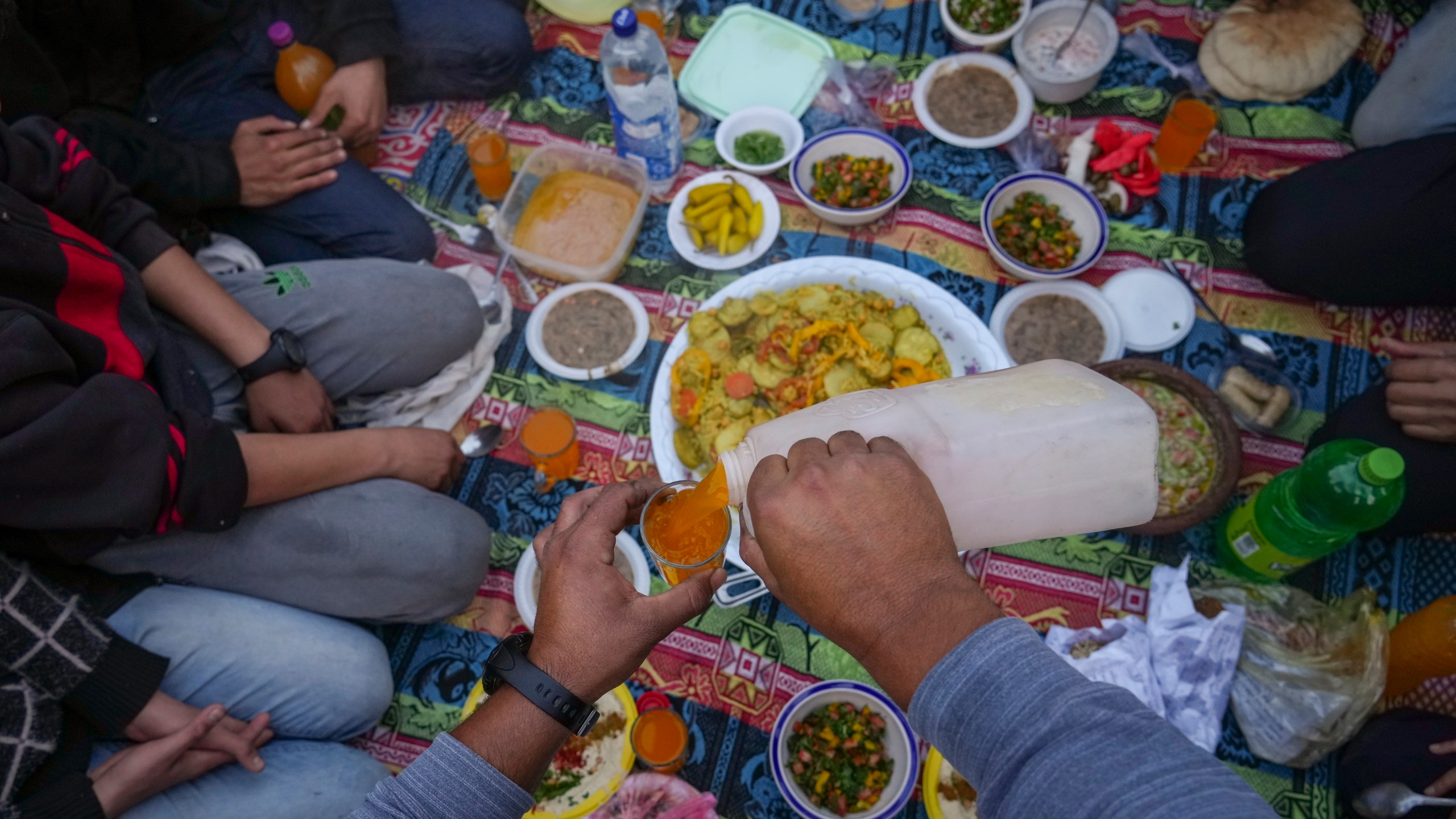 A man serves a juice as Palestinians prepare for Iftar, the fast-breaking meal during Ramadan in a street of the war-devastated Beit Lahia, northern Gaza Strip, Saturday, March 15, 2025. (AP Photo/Jehad Alshrafi)