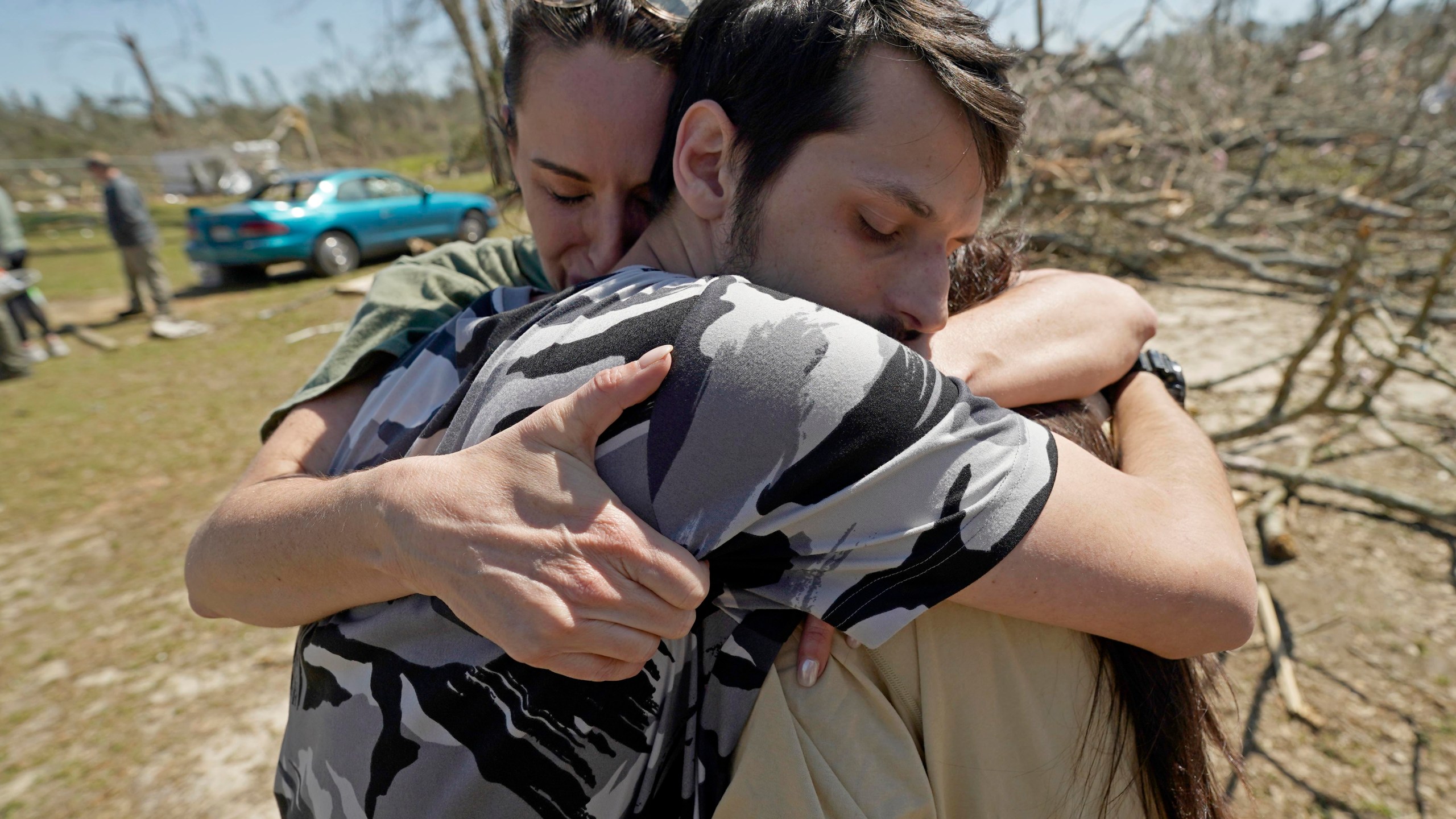 Steve Romero, 23, center, hugs his wife, Hailey Hart, right, and their friend Jessica Soileau, left, after recalling how he, his fiancee and their three dogs rode out Saturday's tornado in their small 1994 Toyota in Tylertown, Miss., on Sunday, March 16, 2024. (AP Photo/Rogelio V. Solis)