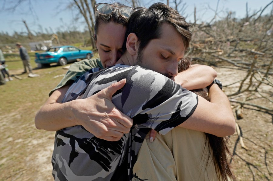 Steve Romero, 23, center, hugs his wife, Hailey Hart, right, and their friend Jessica Soileau, left, after recalling how he, his fiancee and their three dogs rode out Saturday's tornado in their small 1994 Toyota in Tylertown, Miss., on Sunday, March 16, 2024. (AP Photo/Rogelio V. Solis)