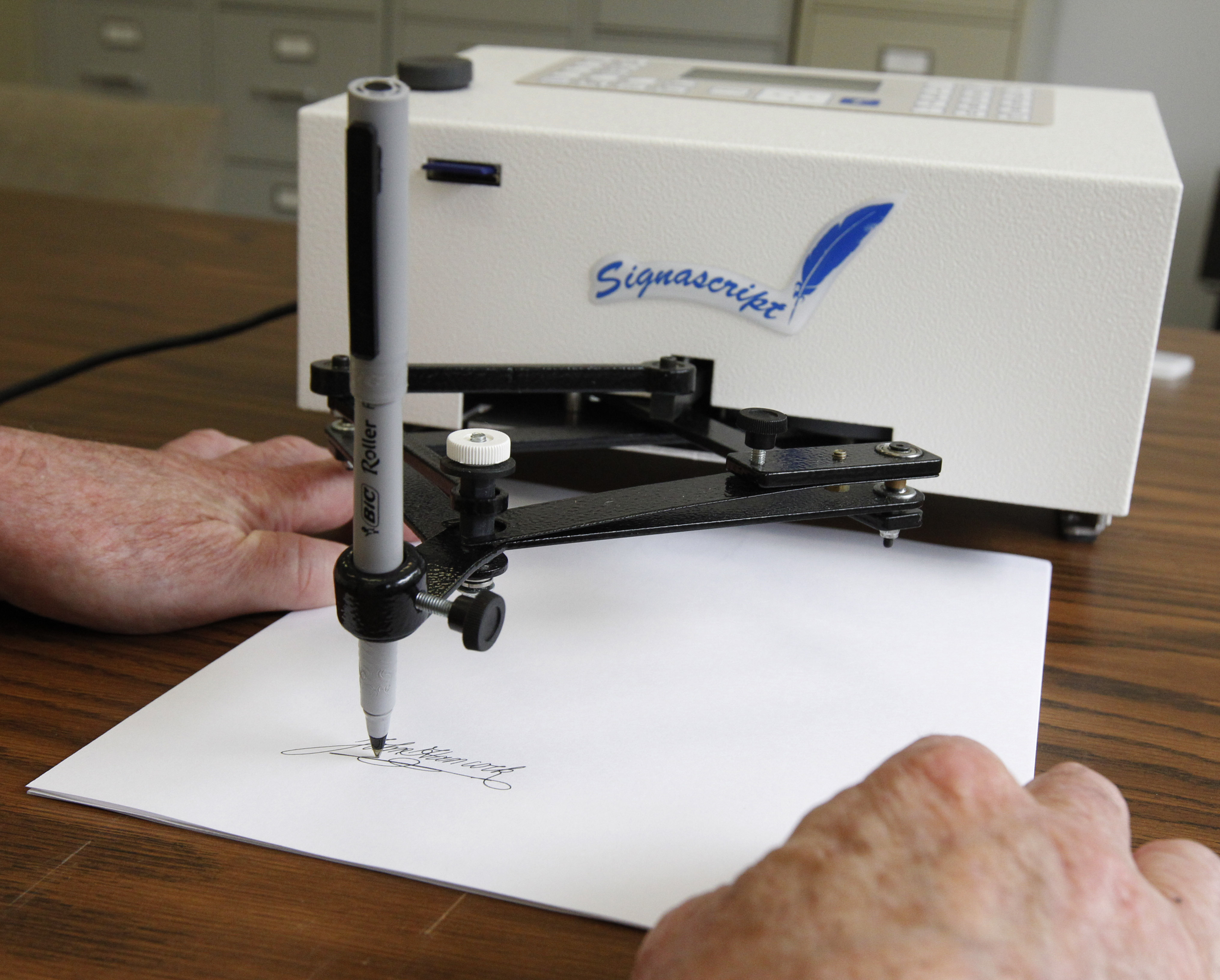 Damilic Corp. president Bob Olding anchors a sheet of paper as the Atlantic Plus, the Signascript tabletop model autopen, produces a signature at their Rockville, Md., office, June 13, 2011. (AP Photo/Manuel Balce Ceneta, File)