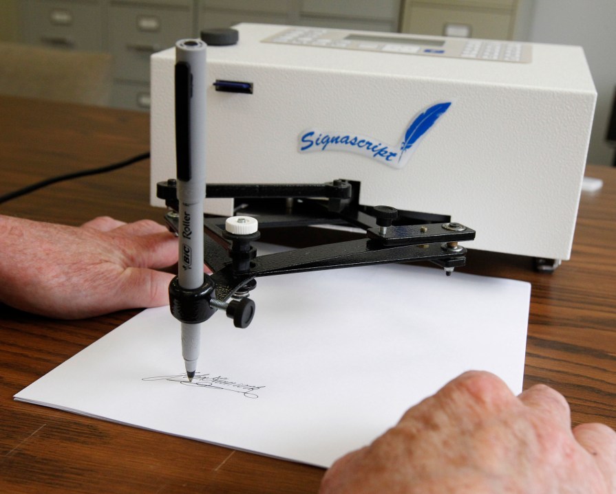 Damilic Corp. president Bob Olding anchors a sheet of paper as the Atlantic Plus, the Signascript tabletop model autopen, produces a signature at their Rockville, Md., office, June 13, 2011. (AP Photo/Manuel Balce Ceneta, File)