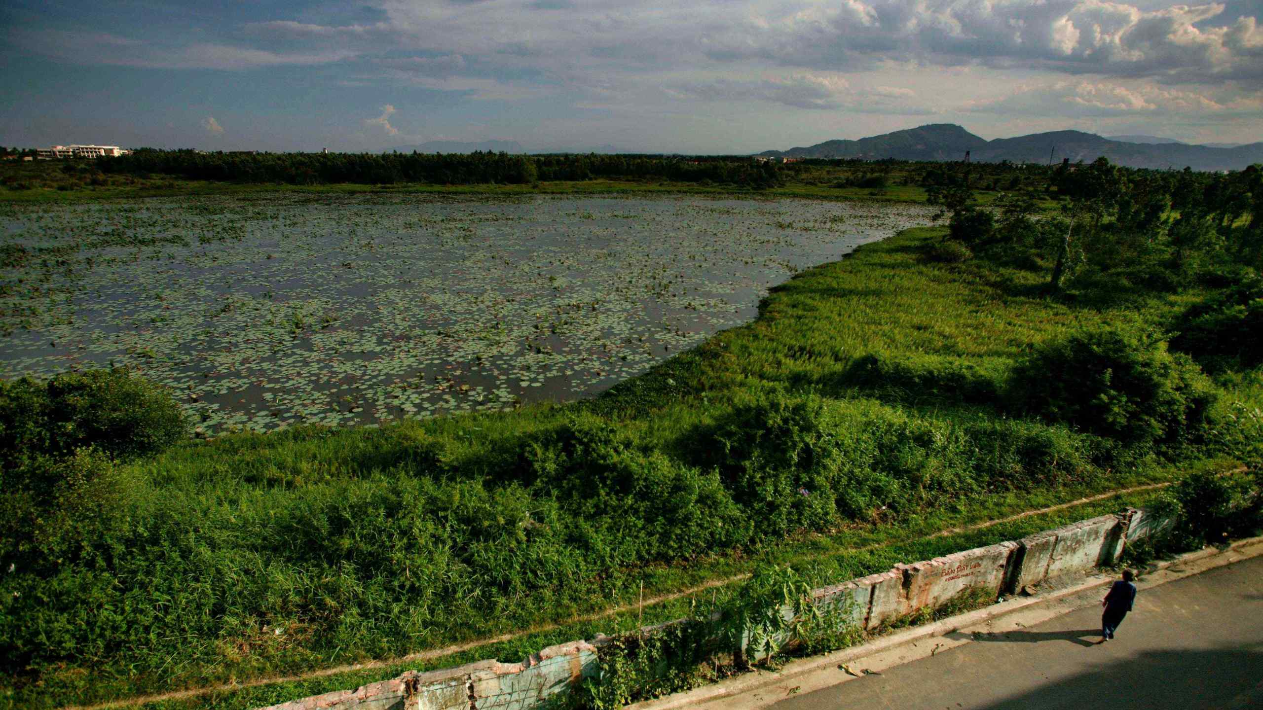 FILE -A woman walks next to a highly contaminated pond around the grounds of the Danang airbase in Danang, Vietnam, May 21, 2007. (AP Photo/David Guttenfelder, File)