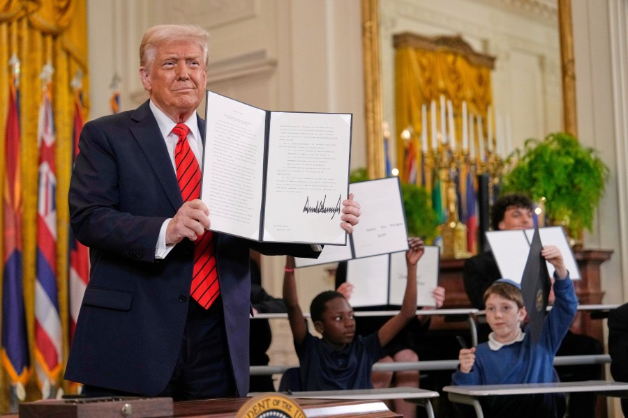 President Donald Trump, left, holds up a signed executive order as young people hold up copies of the executive order they signed at an education event in the East Room of the White House in Washington, Thursday, March 20, 2025. (AP Photo/Ben Curtis)