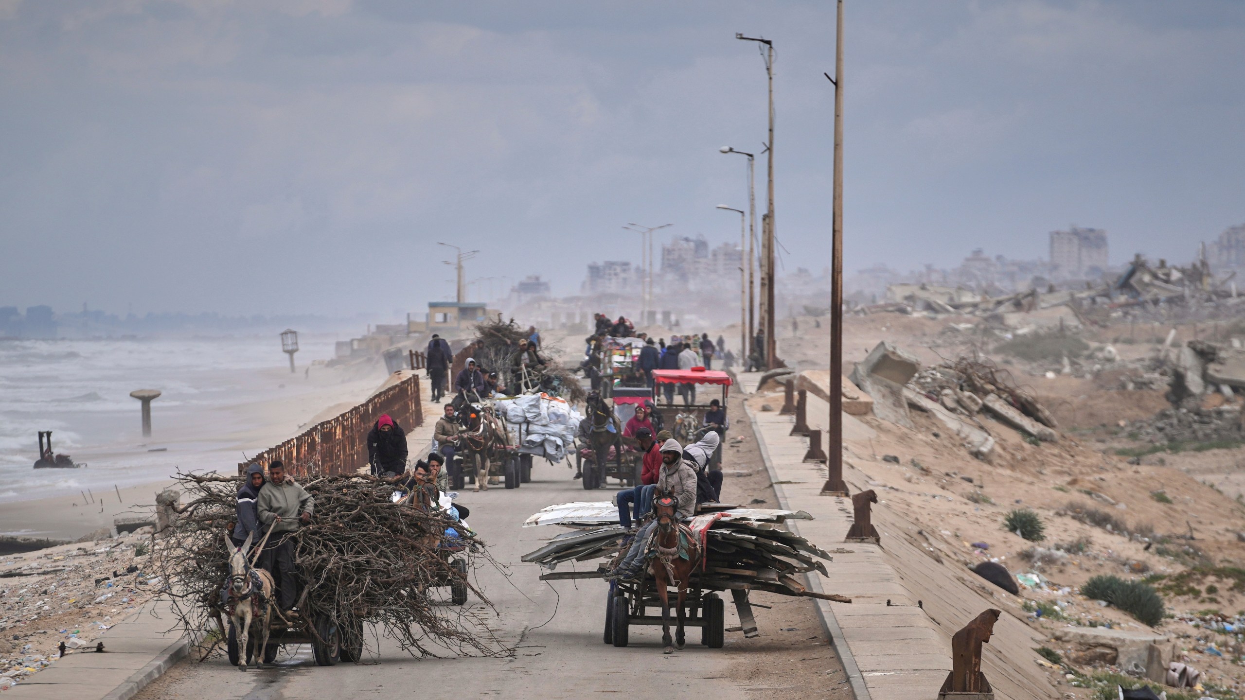 Displaced Palestinians, carrying their belongings, wood and other items, move between southern and northern Gaza along a beach road away from the areas where the Israeli army is operating after Israel's renewed offensive in the Gaza Strip, in the outskirts of Gaza City, Friday March 21, 2025. (AP Photo/Abdel Kareem Hana)