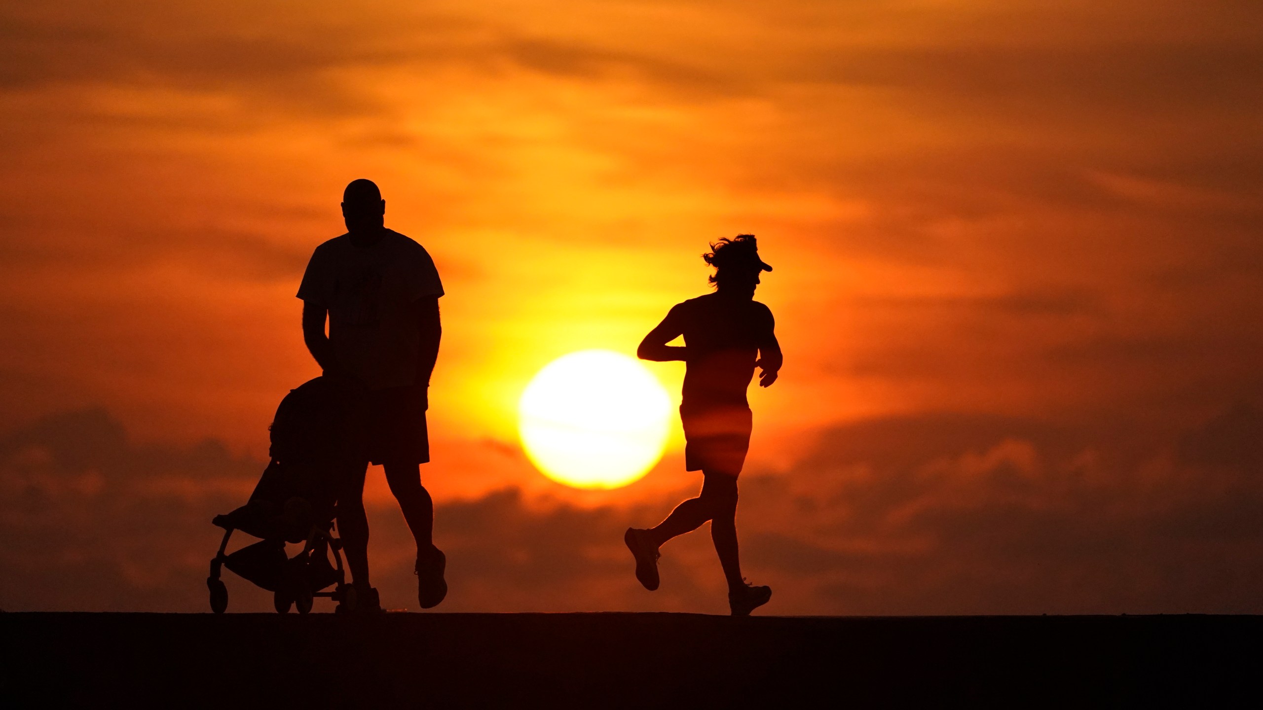 FILE - Walkers and joggers are silhouetted on a jetty as the sun rises over the Atlantic Ocean, Saturday, Sept. 19, 2020, in Bal Harbour, Fla. (AP Photo/Wilfredo Lee, File)