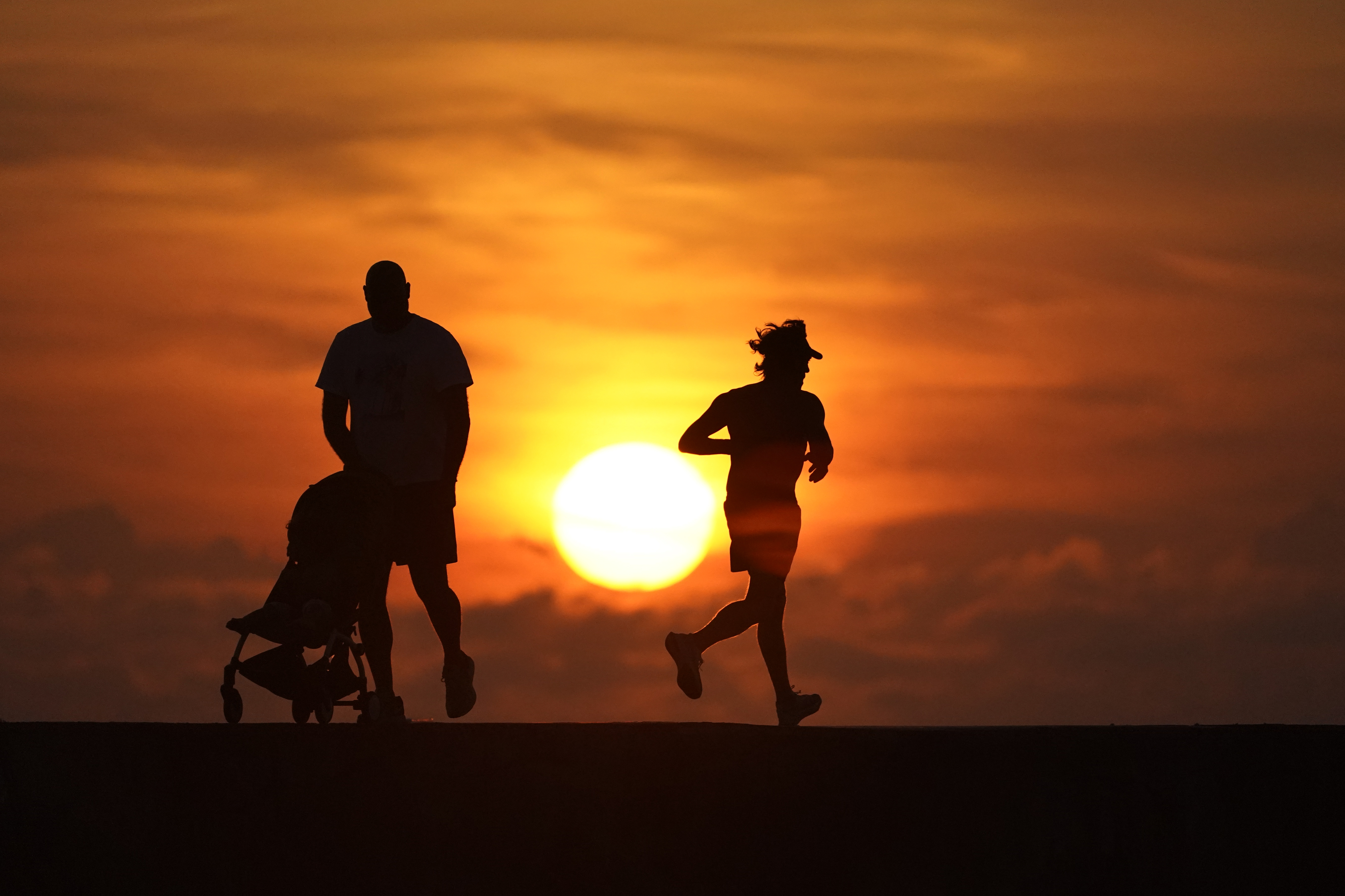 FILE - Walkers and joggers are silhouetted on a jetty as the sun rises over the Atlantic Ocean, Saturday, Sept. 19, 2020, in Bal Harbour, Fla. (AP Photo/Wilfredo Lee, File)