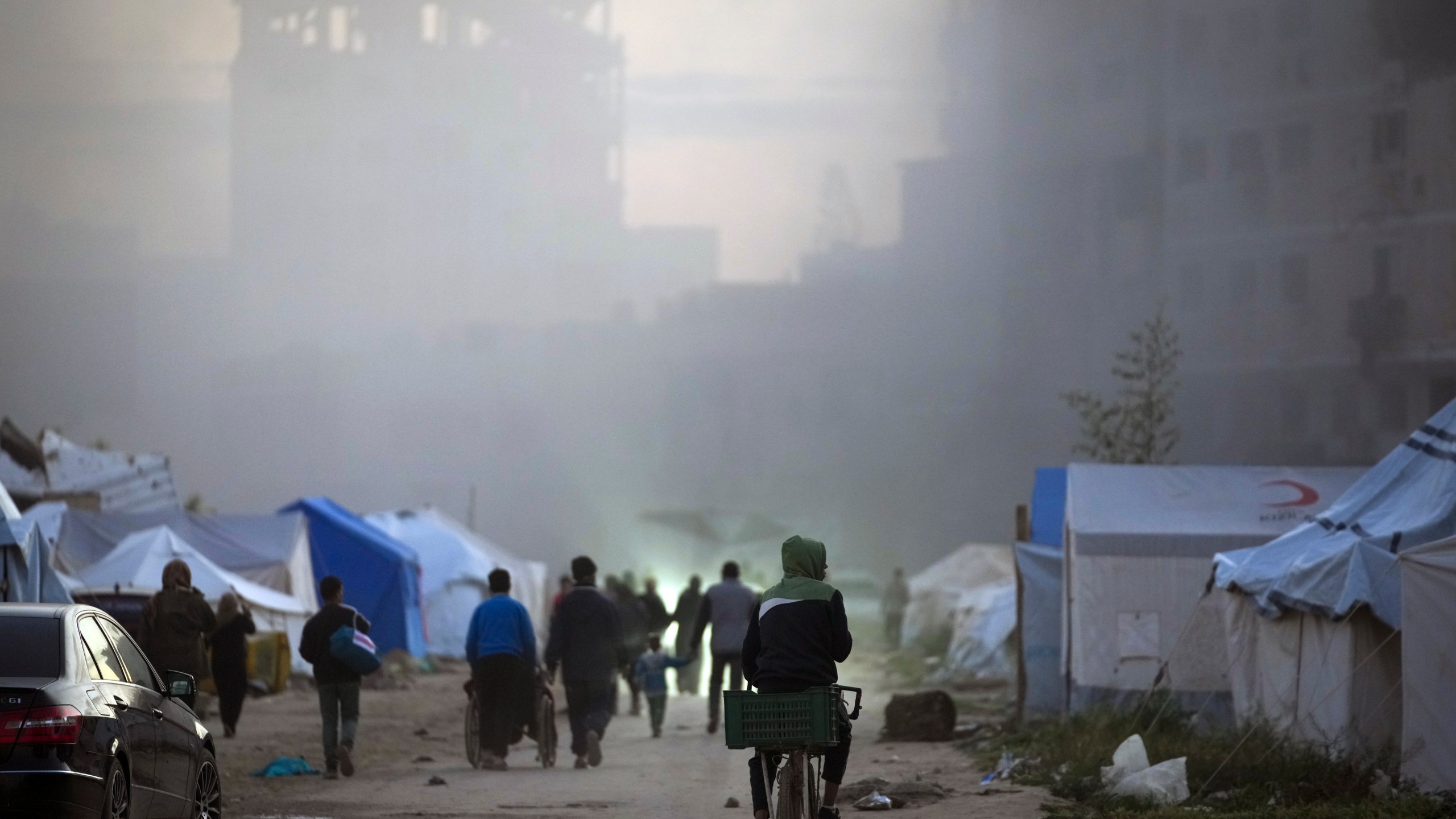 Surrounded by smoke from a nearby Israeli army strike, Palestinians walk past tents in central Gaza City on Saturday, March 22, 2025. (AP Photo/Jehad Alshrafi)