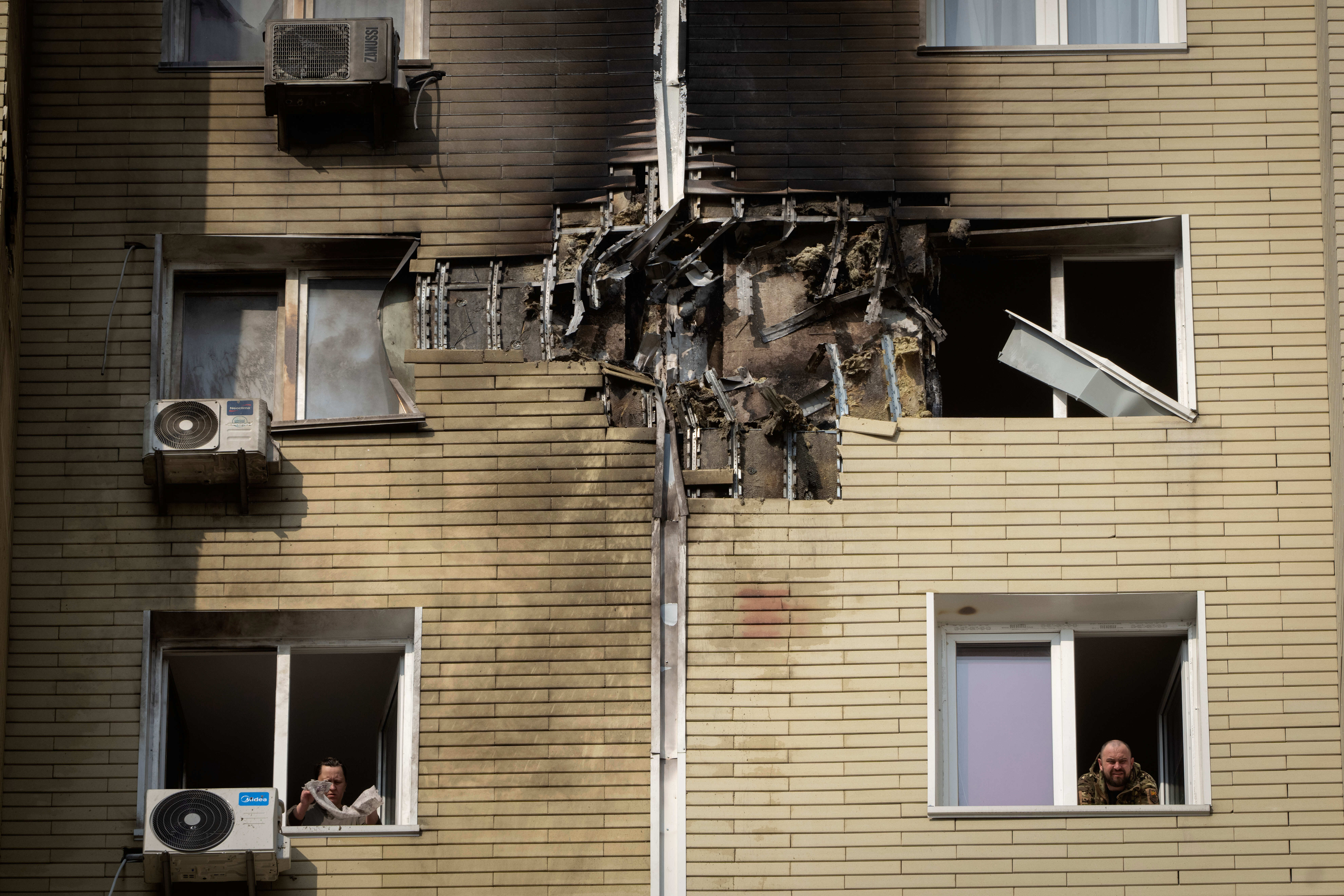 A resident watches as his neighbour cleans up the damaged apartment in a multi-storey house after a Russian night drone attack in Kyiv, Ukraine, Sunday, March 23, 2025. (AP Photo/Efrem Lukatsky)